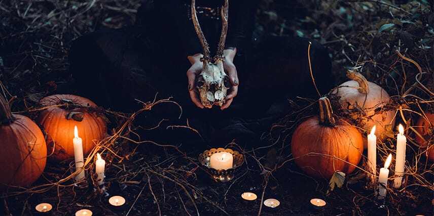 Woman holding a skull surrounded by candles and pumpkins