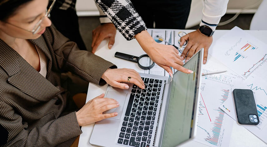 People pointing at laptop with graphs on the table